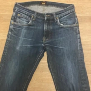 Jeans från Lee straight fit - Säljer ett par mörkblå jeans från Lee, de har hål vid innerbenet men väldigt litet.  Slitningar som kommer från 3 års användning. Jeansen har raka ben och kontrastsömmar i gult. Modellen kallas daren zip fly.