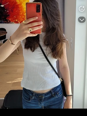 Vit ribbad kortärmad t-shirt - Snygg vit ribbad linnetopp med rund halsringning. Toppen är ärmlös och har en croppad passform som passar perfekt till jeans eller kjol. Enkel och stilren design som är lätt att matcha.