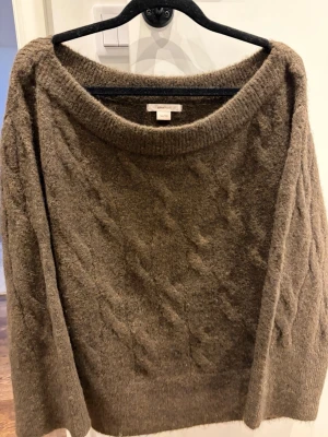 Brun kabelstickad tröja från Gina Tricot - Mysig brun kabelstickad tröja från Gina Tricot  med bred rund halsringning och avslappnad passform. Tröjan har ett klassiskt flätmönster och ribbade muddar. Perfekt för lager på lager under kyliga dagar.