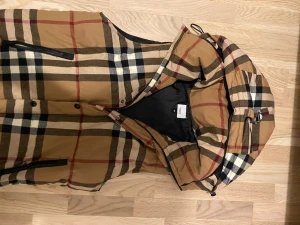 Brunrutig dunväst med huva size s  - Säljer en brunrutig dunväst med klassiskt rutmönster i svart, vitt och rött. Västen har dragkedja, tryckknappar och två fickor framtill samt en stor huva med dragsko. Perfekt för lager på lager och riktigt snygg streetstil.