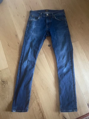 Blå skinny jeans från Lee, Luke - Säljer ett par klassiska blå skinny jeans från Lee. Jeansen har fem fickor, normalhög midja. Midja 76 cm, innerbenslängd 76 cm. Snygg tvätt och smal passform som sitter tajt hela vägen ner. Perfekta till vardagslooken!