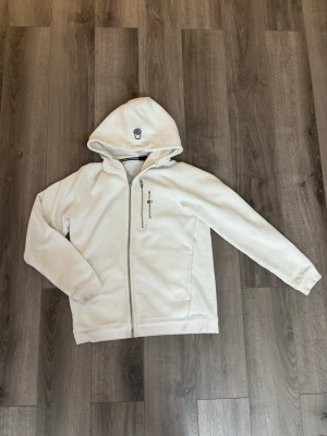 Vit hoodie från Sail Racing kolla beskrivning  - Snygg vit hoodie från Sail Racing med dragkedja framtill och en bröstficka med zip. Märkets logga finns både på huvan och vid bröstet. Hoodien har en klassisk passform och är tillverkad i ett mjukt material som känns skönt mot huden. St är ca 158-164, för att den krympt. Tar emot rimliga bud