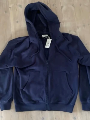 Mörkblå hoodie med dragkedja Vaillent - Mörkblå hoodie från Vaillent med dragkedja framtill, två stora fickor och justerbar huva med snören. Tillverkad i mjukt material som känns skönt mot huden. Perfekt för en avslappnad och stilren look. Priset är inte hugget i sten