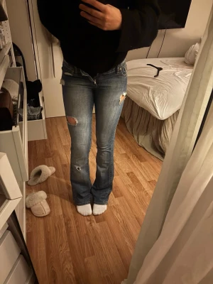 Blå bootcut jeans med slitningar - Vintage jeans från Gina Tricot i blå tvätt med slitningar. Låg midja och lätt utsvängd nertill – riktig Y2K-modell. Sitter snyggt på kroppen (se bild). Midjemått: 38 cm rakt över Innebenslängd: 83 cm Använda men i fint vintage-skick ✨