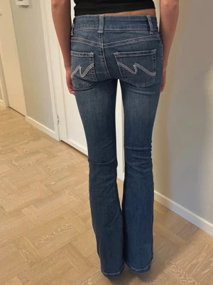 Jeans Nelly low waist stitch stl 34 - Låg midja, utsvängda jeans från Nellie med deras broderade bakfickor. De är knappt använda men har två hårda lim fläckar vid vänster knä. Fläckarna syns knappt, se bild, bortsett från dem är de i toppskick.  Storlek 34 Innermått 81 cm Mått över midjan 34 cm  Obs! De är inte sneda, det var bara modellen som satte på sig de slarvigt.