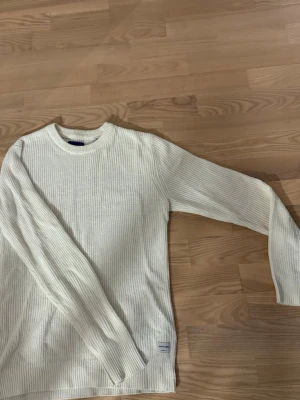 Vit stickad tröja från Jack & Jones - Snygg vit stickad tröja från Jack & Jones Originals. Tröjan har rund halsringning, ribbade muddar och är tillverkad i ett mjukt, grovstickat material. Perfekt för dig som gillar enkel och stilren design.