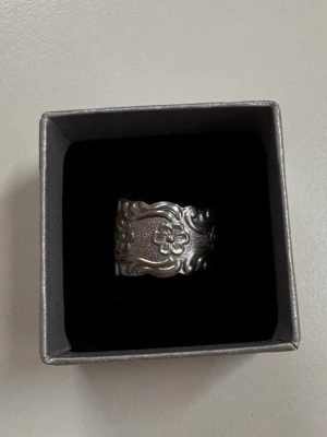 Bred silverring med blommönster tillverkad på återvunna bestick - Unik bred ring i silverfärgad metall med detaljerat blommönster och snirkliga kanter. Ringen har en vintagekänsla och passar perfekt för dig som gillar statement-smycken och vill sticka ut lite extra.