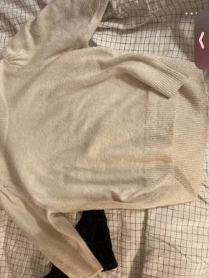 Vit puffärmstickad tröja - Säljer en vit stickad tröja med puffärmar och ribbade muddar vid hals, ärmslut och nederkant. Tröjan har en mjuk struktur och halvlånga ärmar som ger en trendig look. Perfekt att matcha med jeans eller kjol.