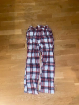 Rutiga pyjamasbyxor i rött och vitt - Mysiga pyjamasbyxor med rött och vitt, och vita  knytband för extra komfort. Perfekta för slappa dagar hemma eller när du vill ha det extra bekvämt på natten.