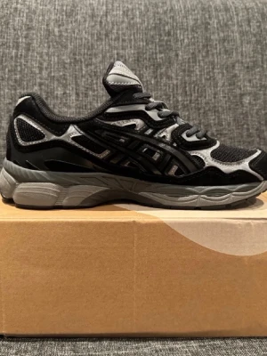 Svarta och grå Asics sneakers - HELT NYA!! Snygga sneakers från Asics i svart och grått med coola detaljer och meshpaneler för extra ventilation. Skorna har snörning och en chunky sula som ger skön komfort. Perfekta för dig som gillar sportig stil och streetwear. Först till kvarn