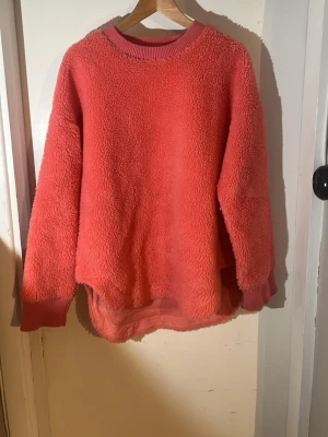 Rosa päls tröja - Mysig rosa päls tröja med rund hals och ribbade muddar vid ärmslut och halsringning. Tröjan har en oversized passform och är gjord i fluffigt, mjukt material som håller dig varm. Perfekt för kyliga dagar och enkel att styla till jeans eller leggings. Den är lite ljusare än på bild.