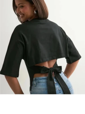 Svart knyt topp - Trendig svart croppad topp med korta ärmar och snygg knytning i ryggen. Perfekt att styla med höga jeans för en cool look. Toppens material känns mjukt och lätt mot huden.