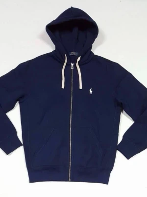 Marinblå hoodie från Polo Ralph Lauren - Snygg marinblå hoodie från Polo Ralph Lauren med dragkedja framtill, vit logga broderad på bröstet och vita snören i huvan. Klassisk passform med kängurufickor och ribbade muddar. Perfekt för en avslappnad och stilren look.