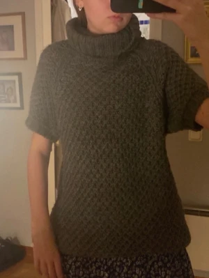 Grå stickad polotröja med kort ärm - Mysig grå stickad tröja med polokrage och korta ärmar. Tröjan har ett snyggt strukturmönster och är lite längre i modellen. Perfekt att styla över en klänning eller med jeans för en trendig look.