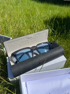 Svarta rektangulära solglasögon AURERA - Snygga solglasögon med svart, rektangulär båge och blåtonade glas. Kommer i ett stilrent fodral och passar perfekt för dig som vill ha en modern och clean look. Bågarna är i metall. Finns ett helt lager så säljer billigt