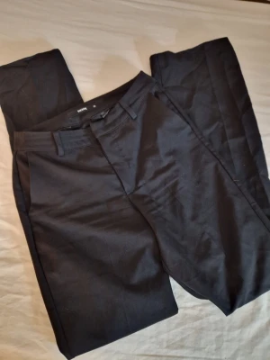 Svarta kostymbyxor - Klassiska svarta kostymbyxor från Bik Bok med raka ben och bälteshällor. Byxorna har två sidofickor fram och två passpoalfickor bak. Perfekta till skjorta eller stickad tröja för en clean look. Fint använt skick. Hund finns I hemmet.