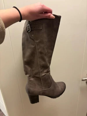 Brun/grå höga boots med klack och spänne - Säljer nu dessa strövar från Jana i Storlek 38, använd någon enstaka gång så nästan som nya 💕