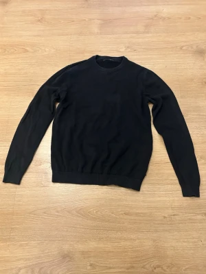 Svart Jack & Jones Tröja - Klassisk svart tröja från Jack & Jones med rund hals och ribbade muddar. Tröjan är långärmad och har en enkel, stilren design som är lätt att matcha. Tillverkad i mjukt material för skön känsla.