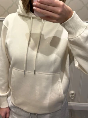 Beige hoodie med ficka och huva - Snygg beige hoodie från Arket med klassisk känguruficka framtill och justerbar huva med dragsko. Tillverkad i mjukt bomullsmaterial och har ribbade muddar vid ärmslut och nederkant. 