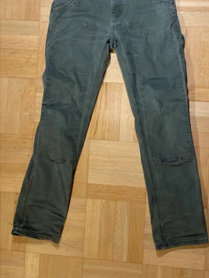 Gröna carpenterbyxor från Dickies - Säljer ett par gröna carpenterbyxor från Dickies med flera  fickor på sidorna och bak. Byxorna har raka ben och klassisk stil, perfekta för en avslappnad och streetig look. Materialet är slitstarkt tyg.