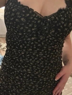 Svart blommig klänning med snörning - Supersöt svart klänning med små vita blommor och snörning vid bysten. Klänningen har smala axelband och figurnära passform. Perfekt för dig som gillar romantisk och trendig stil.