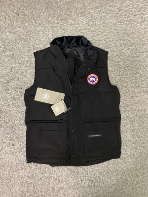 Canada goose väst - Canada Goose väst i storlek M, sprillans ny och aldrig använd. Västen är i perfekt skick utan några defekter och kommer med tags kvar. Klassisk och stilren modell som är lätt att matcha och passar perfekt både till vardags och utomhus – håller värmen utan att kännas klumpig. Hör gärna av dig vid frågor eller om du vill ha fler bilder.