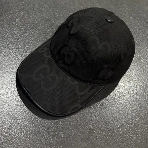 Svart keps från Gucci med GG-mönster - Snygg svart keps från Gucci med diskret GG-mönster över hela kepsen. Klassisk böjd skärm och justerbar rem bak. Materialet är bomull med detaljer i syntet. Perfekt för dig som vill ha en stilren och lyxig look med designer-vibe. Kommer med box och kvitto om det behövs 