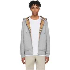 Grå hoodie från Burberry med rutig huva Äkta - Säljer en grå hoodie från Burberry med dragkedja och klassisk rutig huva i beige, svart och röd. Hoodien har snörning vid huvan, två fickor fram och ribbade muddar. Perfekt för dig som vill ha en stilren look med en touch av lyx.