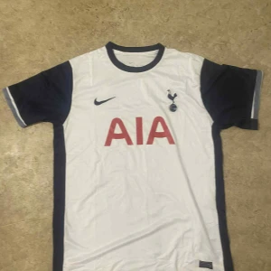 Tottenham Hotspur Nike fotbollströja - Vit Tottenham Hotspur fotbollströja från Nike med mörkblå detaljer på ärmar och sidor. Klassisk rund halsringning, klubbmärke och Nike-logga på bröstet samt röd AIA-sponsor framtill. Tillverkad i lätt och ventilerande material.