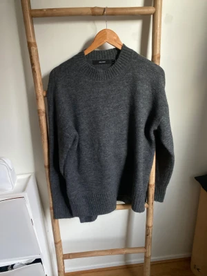 Mörkgrå stickad tröja Vero Moda - Aldrig använd. Mysig mörkgrå stickad tröja från Vero Moda med rund hals och ribbade muddar. Tröjan har lång ärm och slits på sidorna för en chill och loose passform. Perfekt att slänga på sig när det är kallt ute.