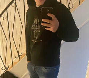 Svart Polo Bear hoodie från Ralph Lauren - Svart hoodie från Ralph Lauren med Polo Bear-tryck på bröstet. Tröjan har huva med snörning och ribbade muddar. Björnen på framsidan har en stickad tröja med vintermönster. Perfekt för dig som gillar klassisk streetstyle med en twist.