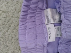 Ljuslila mjukisbyxor från H&M Move - Säljer ett par ljuslila mjukisbyxor från H&M Move med bred resår i midjan och snörning framtill. Byxorna har en loose passform och raka ben, tillverkade i mjukt syntetmaterial som är skönt mot huden. Perfekta för chill eller träning. 