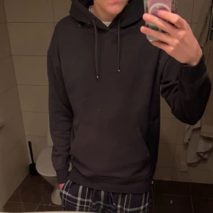 Svart hoodie från Jack & Jones L - Svart hoodie från Jack & Jones i storlek L. Klassisk modell med huva och snörning, stor magficka framtill och ribbade muddar vid ärmslut och nederkant. Mjuk insida i bomullsmix. Jättefint skick på den och den har inte använts så mycket. Hör av er om ni har frågor!