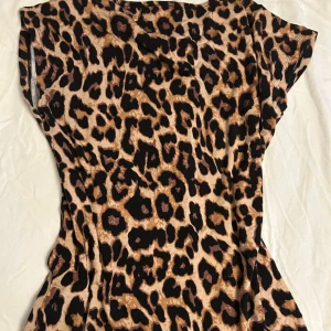 Leopardmönstrad t-shirt - Säljer en snygg t-shirt med leopardmönster i beige, svart och bruna toner. T-shirten har rund hals och är kortärmad, med en figurnära passform som framhäver siluetten. Perfekt för dig som gillar att sticka ut med djurmönster.