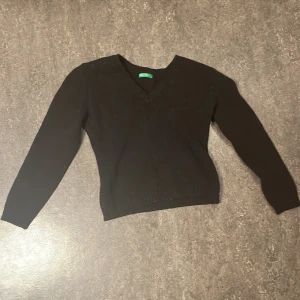 Svart v-ringad stickad tröja Benetton - Svart stickad tröja från Benetton med v-ringad hals och långa ärmar. Tröjan har ribbade muddar vid ärmslut och nederkant, vilket ger en snygg och enkel look. Perfekt för dig som gillar klassisk stil med en modern touch.