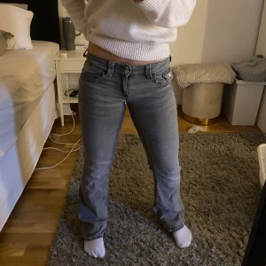 Grå bootcut jeans från Gina Tricot - Snygga grå jeans från Gina Tricot med bootcut passform och låg midja. Jeansen har dubbla knappar fram, klassiska fickor och en cool fickdetalj med lock. Materialet är mjukt jeans-tyg som sitter bekvämt och ger en schysst siluett. 