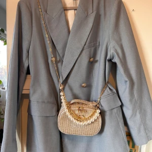 Ljusgrå kavaj från H&M, storlek M - Snygg ljusgrå kavaj från H&M i klassisk modell med dubbelknäppning och guldfärgade knappar med emblem. Kavajen har breda slag, fickor med lock och en stilren passform. Perfekt för dig som gillar en clean och sofistikerad look.