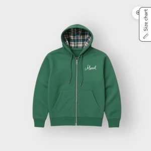 Grön hoodie från Leon Marcél - Grön hoodie från Leon Marcél Archive Collection med vit broderad logga på bröstet. Utsidan är slät och insidan av huvan har ett rutigt foder i grönt, vitt och brunt. Tröjan har dragkedja, och två stora fickor framtill.