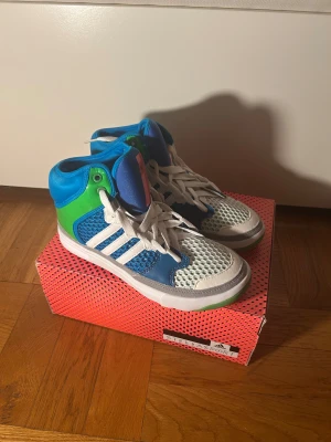 Adidas Stellasport blå/gröna sneakers - Säljer ett par Adidas Stellasport sneakers i storlek 38. Skorna har en cool high-top design med blått och grönt syntetmaterial, vit mesh och klassiska vita ränder. De har snörning och platt sula, perfekt för dig som gillar sportig och färgstark stil. (Ordinare pris 1200kr) Strl 37 1/3, 38, 38,5 finns i lager vid förfrågan