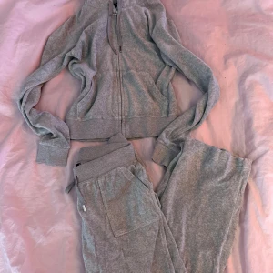 Grå mjukissett Juicy Couture S - Grå mjukissett från Juicy Couture i storlek S. Byxorna har bred resår i midjan med snörning, praktiska fickor fram och bak med lock och knappar. Mjukt material som är perfekt för chill och häng. Klassisk Juicy Couture-logga på fickan.