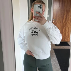 Vit sweatshirt med tryck (ny) - Vit sweatshirt från Divided H&M med svart broderat tryck på bröstet. Rund hals, ribbade muddar och mjukt fleecematerial på insidan. Finns en liten prick på vänster ärm, borde gå bort i tvätt. Blev aldrig använd - ej nopprig, fortfarande mjuk på insidan.