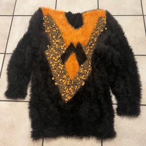 Svart och orange mohair tröja - Unik och iögonfallande tröja i svart och orange med pälsig textur. Tröjan har ett geometriskt mönster framtill och långa ärmar. Perfekt för att sticka ut i mängden!