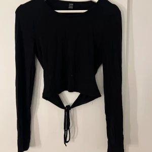 Svart långärmad topp med knytning - Svart långärmad topp från SHEIN med rund hals och croppad passform. Toppen har en knytning i ryggen! Säljer då den inte kommer till användning!✨💕