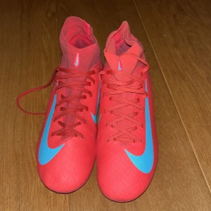 Röda Nike Mercurials - Säljer ett par riktigt snygga röda Nike fotbollsskor med högt skaft och blå Nike. Mycket bra skick inte mycket fel med fotbollsskorna