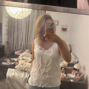 Vit linnetopp med spetsdetalj - Säljer en vit linnetopp med snygg spets runt halsringningen. Toppen är ärmlös och har en avslappnad passform som gör den enkel att styla med jeans eller kjol. Perfekt för varma dagar och har en feminin touch tack vare spetsen.