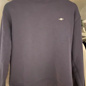 Mörkblå sweatshirt från Gant - En stilren mörkblå sweatshirt från Gant med diskret logga broderad på bröstet. Tröjan har rund halsringning och långa ärmar. Perfekt för dig som gillar en enkel och klassisk look. Typ aldrig använt 