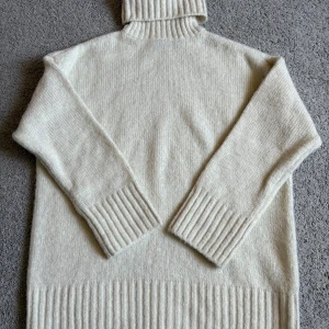 Vit polotröja från Pieces - Mysig vit polotröja från Pieces med bred ribbstickad krage, ärmslut och nederkant. Tröjan är stickad i ett mjukt material och har lång ärm. Perfekt för kyliga dagar och enkel att styla med dina favoritjeans.