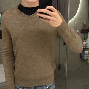 Stickad Morris tröja - Snygg beige stickad tröja från Morris med v-ringning och diskret blå logga på bröstet. Den är i storlek L men är liten i storleken vilket gör att den passar bäst för dig som brukar ha S/M. Jag är 185 cm och väger ca 70 kg. Den är i bra skick förutom en pytte liten effekt vid armen som man kan se på bild 4.