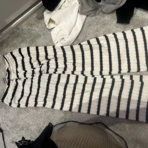 Randiga stickade byxor från Gina Tricot - Säljer ett par vita och svarta stickade byxor från Gina Tricot i storlek XS. Byxorna har breda svarta ränder, är vida i modellen och har en mjuk, virkad känsla. Perfekta för dig som gillar en chill och trendig stil.