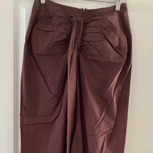 Brun långkjol med slits från Gina Tricot - Säljer en brun långkjol från Gina Tricot i storlek M. Kjolen har en snygg slits framtill och draperad detalj i midjan. Tillverkad i ett lätt bomullsliknande material och stängs med dragkedja bak. Perfekt för dig som gillar stilrena och trendiga plagg.